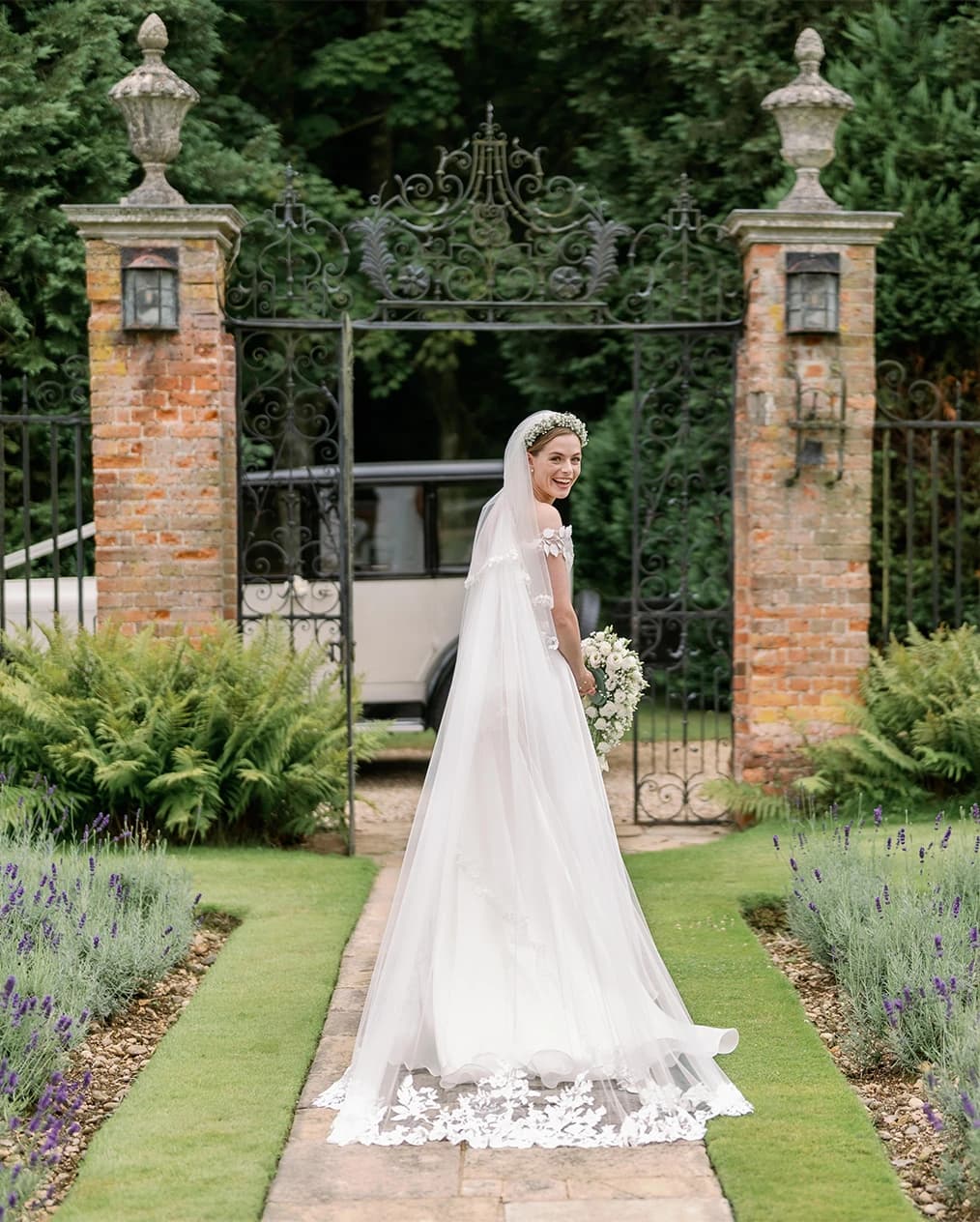 Bride walks through the garden towards the vintage wedding car