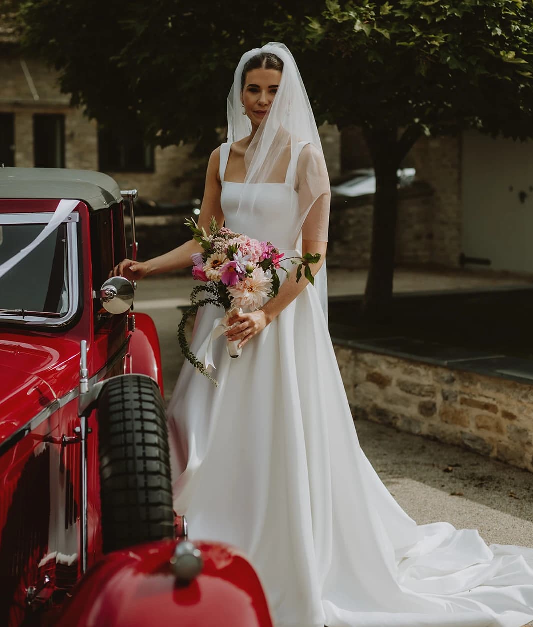 Bride stepping from a red vintage Alvis holding her wildflower bouquet