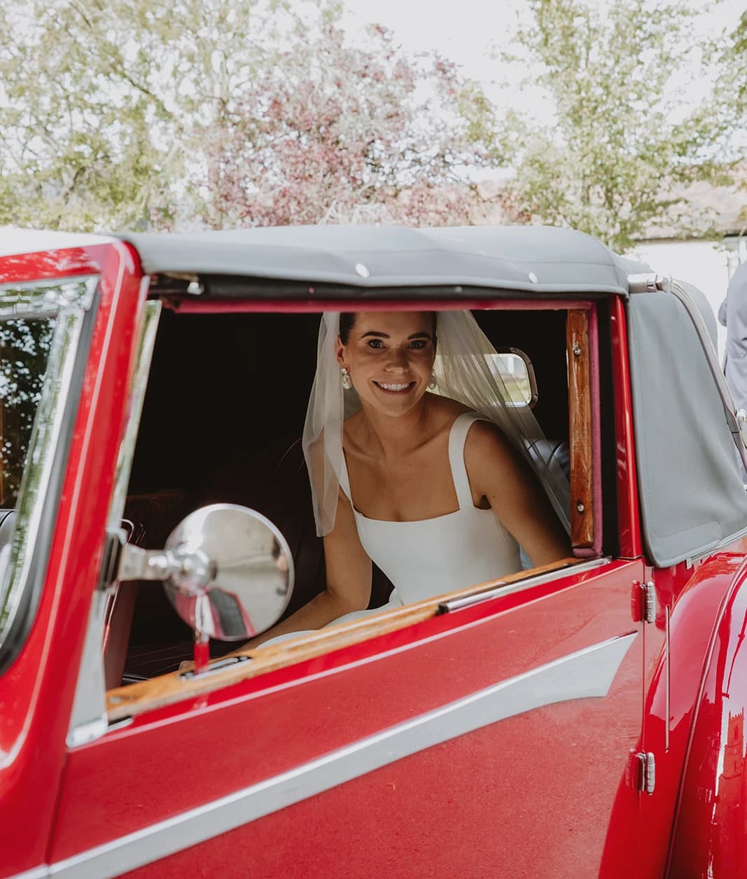 Smiling bride sitting in the red vintage Alvis on arrival at the church