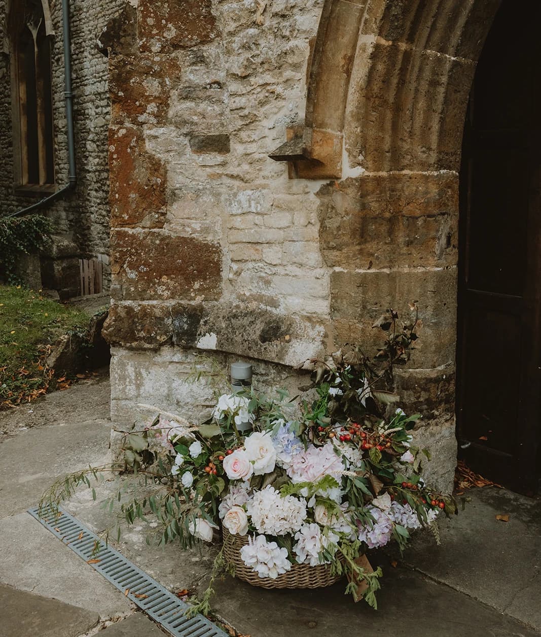 Basket of pastel hydrangeas and roses beside the stone church doorway