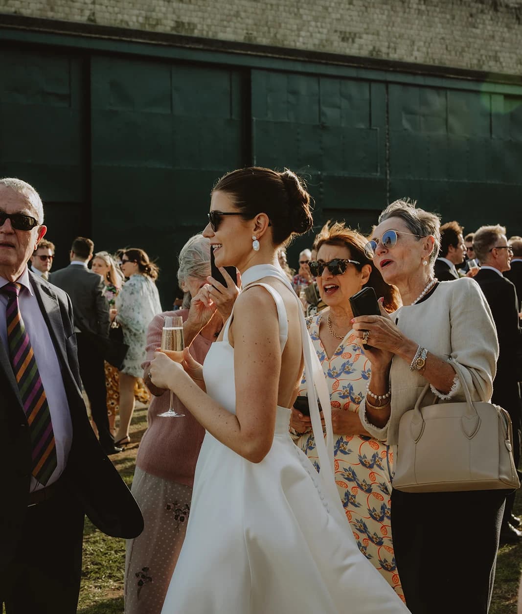 Bride in a low-back wedding dress chatting with guests at the airfield reception 