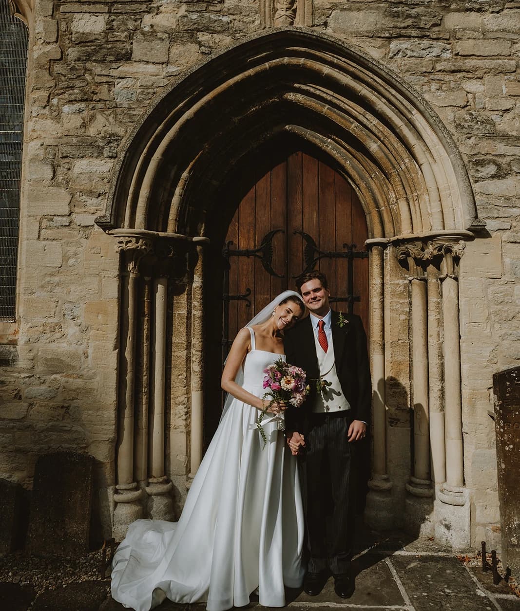 Bride and groom posing beneath the Gothic arched door of St Edburg's Church