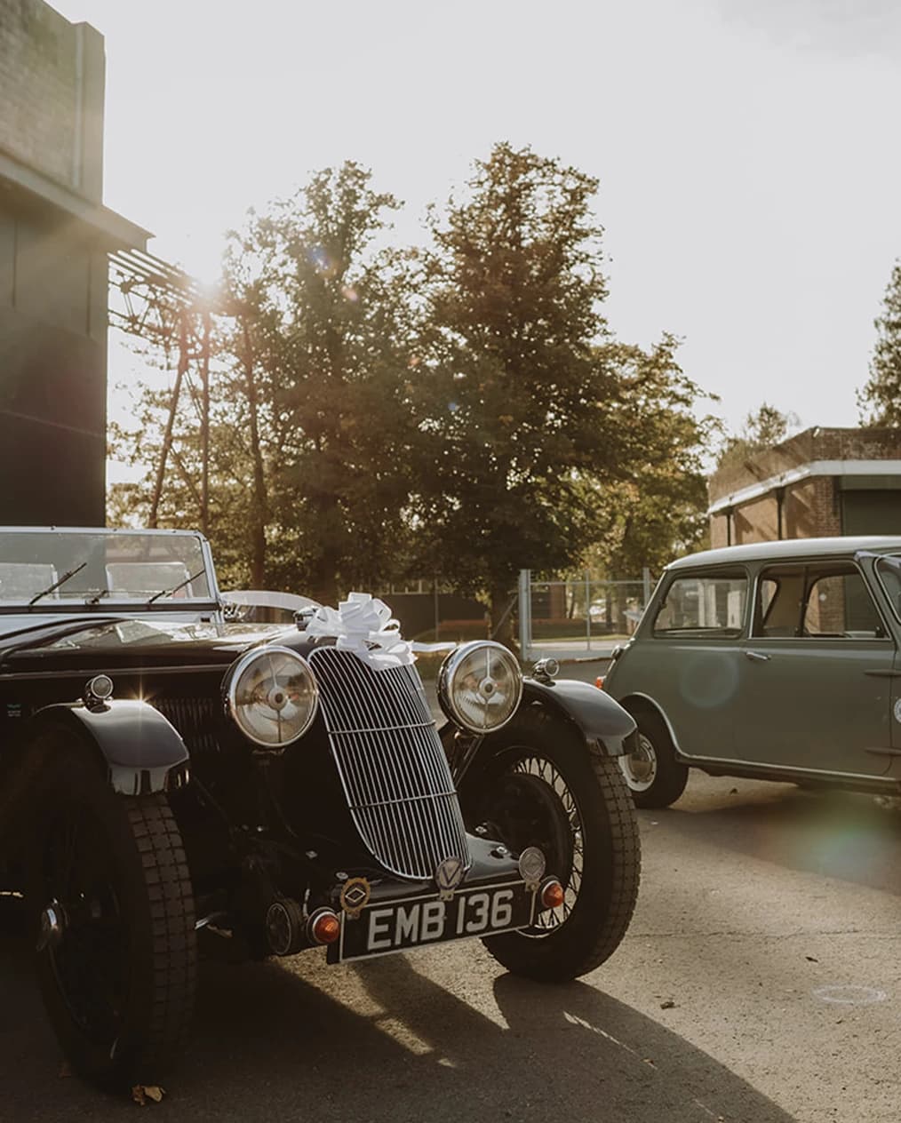 Classic cars and a vintage Mini lined up in the sunshine outside the hangars