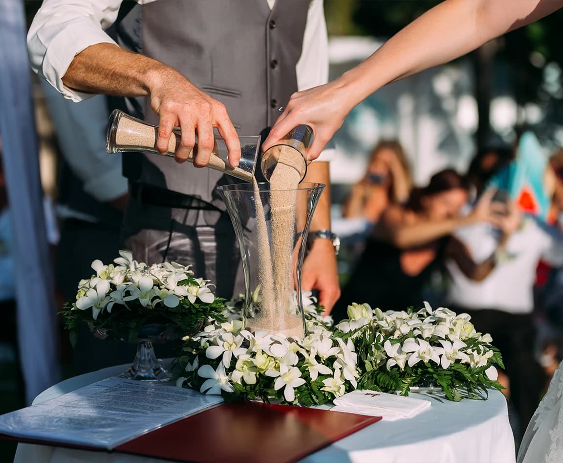 Bride and groom pour sand into a glass vessel during their unity sand ceremony