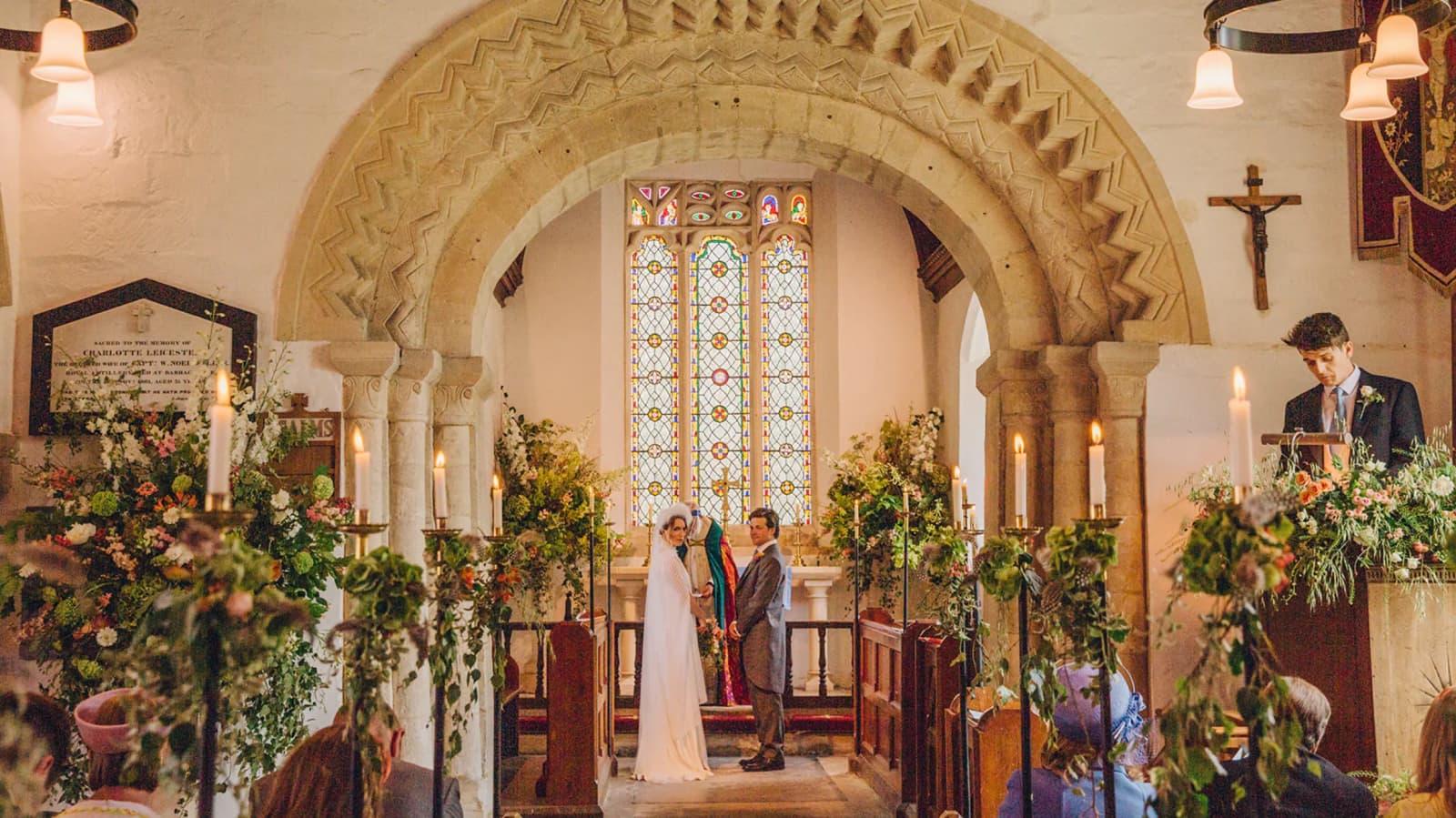 A carved Norman arch frames the couple at the altar, the chancel filled with autumnal flowers and candles