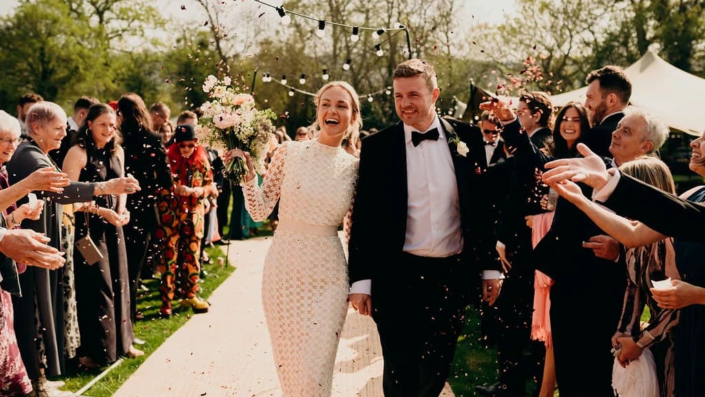 Guests line the path under festoon lights, showering the couple with confetti at an outdoor wedding.